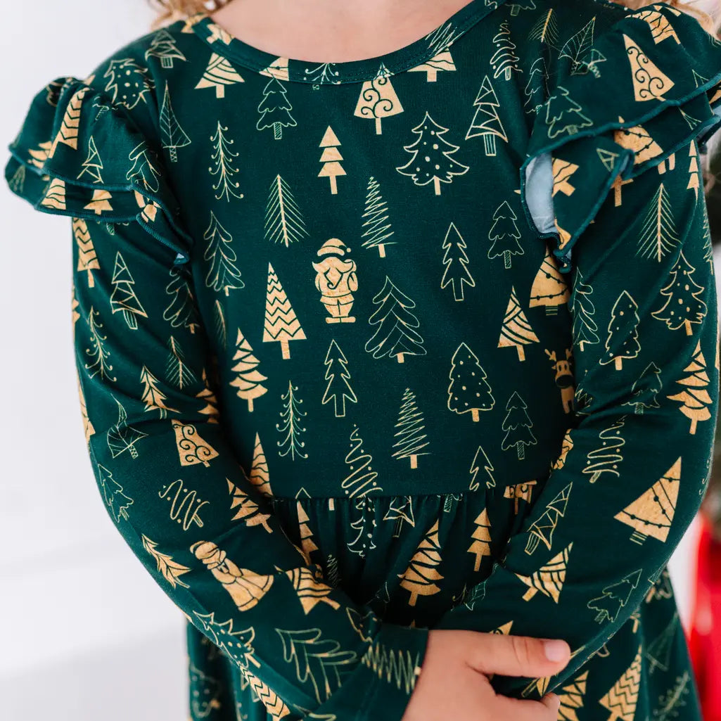Close up of the front of a long sleeve twirl dress with flutter ruffles at the shoulders in a dark green print of gold Christmas trees.